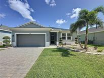 Charming home featuring a well-manicured lawn, paver driveway, and beautiful landscaping with a mature palm tree at 655 Conservation Blvd, Groveland, FL 34736
