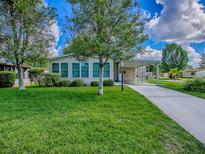 Well-maintained home featuring a spacious front yard, covered carport, and lush landscaping under a bright, partly cloudy sky at 601 Jason Dr, The Villages, FL 32159
