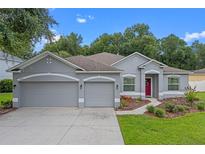 Beautiful single-story home featuring a three-car garage, landscaped yard, and a charming red front door at 1702 Hoofprint Ct, Fruitland Park, FL 34731