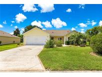 Charming home with a well-manicured lawn, mature trees, and a long driveway leading to a two-car garage at 2450 Merida Cir, The Villages, FL 32162