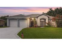 Charming single-story home with a well-manicured lawn, double garage, and beautiful landscaping at sunset at 22125 Draw Bridge Dr, Leesburg, FL 34748
