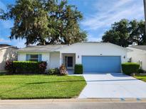 Charming single-story home with a well-manicured lawn, blue garage door, and lush landscaping at 651 Timbercrest Dr, Leesburg, FL 34748