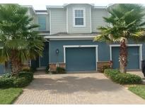Charming townhome featuring a blue exterior, two-car garage, and lush palm trees at 1867 Holden Ridge Lane, Clermont, FL 34715