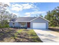 Charming single-story home with a well-manicured lawn, attached garage, and bright red front door at 700 Fisher Rd, Ocklawaha, FL 32179