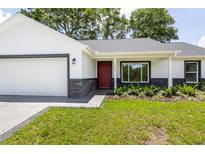 Charming single-story home featuring a well-manicured lawn, stone accents and a welcoming red front door at 13050 Ne 7Th Loop, Silver Springs, FL 34488