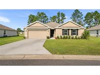 Tan house with a two-car garage and well-manicured lawn at 141 Hickory Course Cir, Ocala, FL 34472