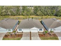 An aerial view of a white duplex with manicured landscaping, brick driveways, and a wooded backdrop at 5341 Nw 48Th Pl, Ocala, FL 34482