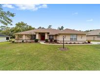 Charming single-story home with a manicured lawn, tasteful landscaping and a vibrant red front door at 10458 Sw 52Nd Ct, Ocala, FL 34476