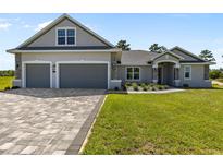 Beautiful home featuring a gray exterior, two-car garage, brick paved driveway, and lush green lawn at 17781 Sw 72Nd Street Rd, Dunnellon, FL 34432
