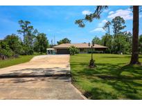 Charming single-story home featuring a lush green lawn, mature trees, and a long private driveway at 7591 Limonia Dr, Indian Lake Estates, FL 33855