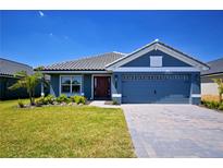 Charming single-story home with a blue exterior, well-manicured lawn, and a gray tiled roof under a clear blue sky at 5120 Villa Crest Way, Auburndale, FL 33823
