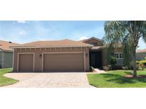 Tan two-car garage home with a landscaped lawn and palm tree at 5269 Pebble Beach Blvd, Winter Haven, FL 33884