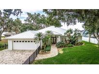 Beautiful home with a white exterior, metal roof, brick driveway, and mature landscaping in a lakeside setting at 739 Swann Dr, Lakeland, FL 33809