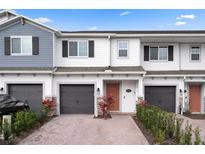 Charming townhome exterior with a gray garage door, brick driveway, and well-manicured landscaping at 5002 Rain Shadow Dr, St Cloud, FL 34772