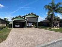 Well-maintained exterior with a brick driveway leading to a three-car garage and lush landscaping at 585 Meandering Way, Polk City, FL 33868