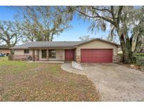 Charming single-story home featuring a well-manicured lawn, mature trees, and a red two-car garage door at 3511 Southcrest Blvd, Lakeland, FL 33812