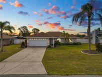 Charming single-story home with well-manicured lawn, mature palm trees, and a two-car garage under a colorful sunset sky at 5252 Montserrat Dr, Lakeland, FL 33812