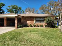 Charming brick home with a well-manicured lawn and covered carport under a clear, blue sky at 561 Lake Mystic Ln, Lakeland, FL 33813