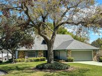 Charming single-story home with a stone facade, attached garage, mature trees, and lush green lawn at 1842 Pinnacle Dr, Lakeland, FL 33813