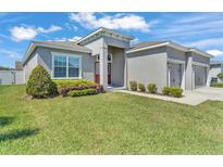 Charming single-story home with well-manicured lawn, gray paint, and a three car garage at 6185 Gracie Pl, Lakeland, FL 33812