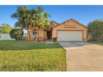 Inviting single-story home featuring a two-car garage, lush lawn, and mature palm trees enhancing its curb appeal at 404 Emerald Cove Loop, Lakeland, FL 33813