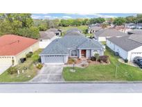 Charming single-story home with a well-manicured lawn, gray stucco and decorative landscaping under a partly cloudy, blue sky at 7335 Beaumont Dr, Lakeland, FL 33810
