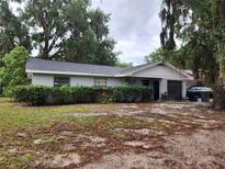 Cozy single-story home features a gray brick facade, dark roof, attached garage, and lush shrubbery at 930 E Tee Cir, Bartow, FL 33830