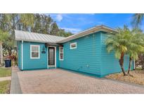 Charming blue home features a brick driveway and a metal roof surrounded by palm trees at 3243 Red Tail Hawk Dr, Polk City, FL 33868