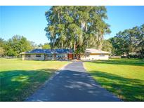 Inviting single-story home featuring a large front yard, mature trees and an orange front door at 5121 Shady Oak S Dr, Lakeland, FL 33810