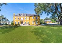 Stately yellow three-story home with large lawn, balcony, dormer windows, and mature trees on a sunny day at 3020 Crews Lake Dr, Lakeland, FL 33813