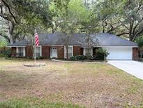 Charming brick home with a well-manicured lawn, mature trees, and an American flag at 6116 Sweet Gum Run, Bartow, FL 33830