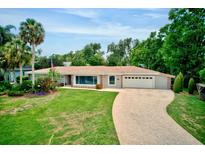 Beautiful single-story home with a well-manicured lawn, brick driveway, and lush tropical landscaping at 1235 Lake Point Dr, Lakeland, FL 33813