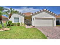 Charming single-story home featuring a manicured lawn, palm trees, and a brick driveway leading to a two-car garage at 4188 Muirfield Loop, Lake Wales, FL 33859