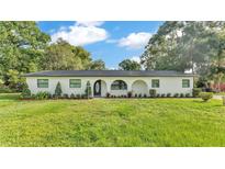Charming single-story home featuring a white facade, arched entryway, and lush green lawn with mature trees at 3235 Sandpiper Ln, Mulberry, FL 33860