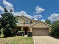 Inviting two-story home featuring a well-manicured lawn, mature trees, and a neutral color scheme under a sunny blue sky at 4665 Sw 40Th Pl, Ocala, FL 34474