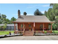 Charming log cabin featuring a covered porch, stone chimney, and landscaped front yard at 2536 Paige Ave, New Smyrna Beach, FL 32168