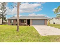 Front view of a single-story house with a gray garage door and a well-maintained lawn at 1820 Sabal Palm Dr, Edgewater, FL 32132