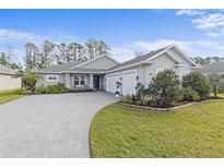 Gray house with three-car garage, paver driveway, and landscaped yard at 3309 Modena Way, New Smyrna Beach, FL 32168