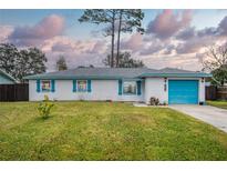 White brick ranch house with teal accents, a blue garage door, and a well-maintained lawn at 2325 Willow Oak Dr, Edgewater, FL 32141