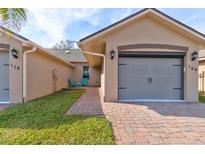 Tan house exterior with gray garage door, brick pavers, and small courtyard at 108 Tuscany Villas Dr # 15, Edgewater, FL 32141