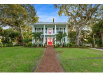 Two-story light blue house with red door, brick pathway, and lush landscaping at 504 N Riverside Dr, New Smyrna Beach, FL 32168