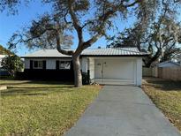 Charming single-story home featuring a metal roof, white siding and a spacious front yard with mature landscaping at 128 Orange Ave, Edgewater, FL 32132