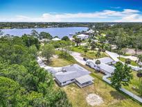 Expansive aerial view of a single story home next to a lake surrounded by lush greenery and an inviting neighborhood at 1812 Bayview Dr, New Smyrna Beach, FL 32168