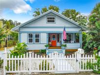 Charming light blue cottage featuring a white picket fence, orange door, and well-maintained landscaping at 216 Murray St, New Smyrna Beach, FL 32168