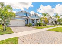 Charming two-story home with a well-manicured lawn, inviting porch, and two-car garage with a brick paver driveway at 219 Venetian Palms Blvd, New Smyrna Beach, FL 32168