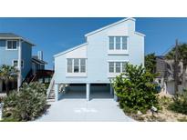 Charming two-story beach house with a light blue exterior, elevated on stilts, with lush landscaping at 6871 S Atlantic Ave., New Smyrna Beach, FL 32169