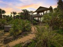 Inviting multi-story home surrounded by lush tropical landscaping and a sandy path with mature foliage at 1421 N Atlantic Ave, New Smyrna Beach, FL 32169