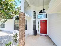 Inviting white home exterior featuring a red front door, decorative brick pillar, and manicured landscaping at 1941 Spruce Creek Lndg, Port Orange, FL 32128