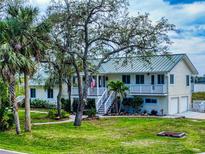 Charming two-story home boasting lush landscaping, a metal roof, and inviting staircases to elevated porches at 2950 Sunset Dr, New Smyrna Beach, FL 32168