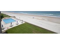 Aerial view of a community pool near a sandy beach, with lounge chairs and tables with umbrellas at 4435 S Atlantic Ave # 416, Port Orange, FL 32127